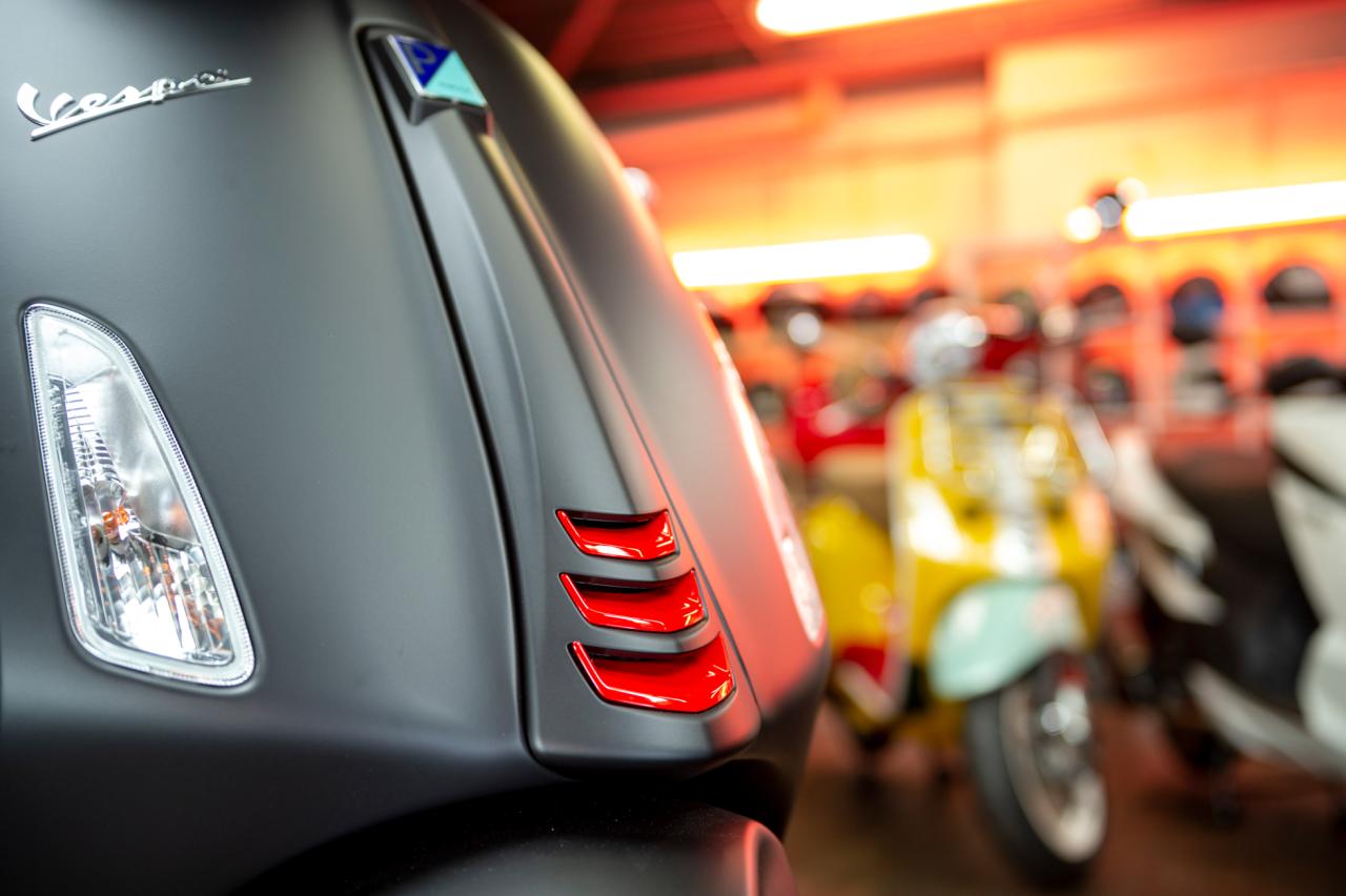 Schwarze Vespa, im Hintergrund stehen weitere Roller.